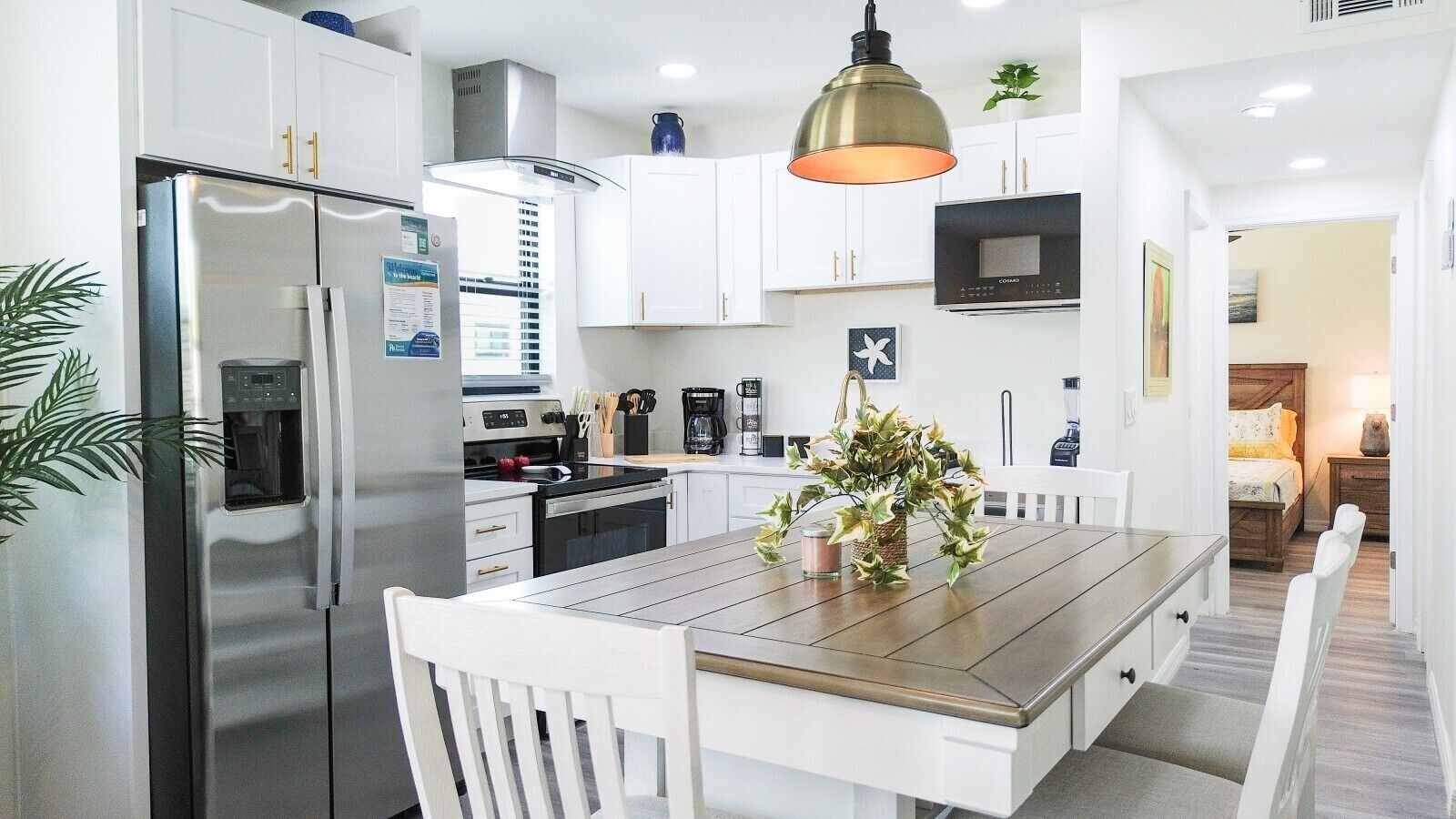 A modern kitchen with white cabinetry, stainless steel appliances, and a wooden dining table.