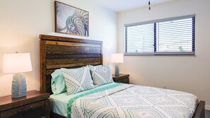 A bedroom with a wooden headboard, a patterned bedspread, two bedside lamps, and a window with blinds. - Nautilus Island Compound - Roof Deck - Sleeps 16 (Treasure Island)