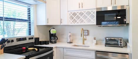 A modern kitchen with white cabinets, a black stove, a coffee maker, a toaster, and a sink with a gold faucet.