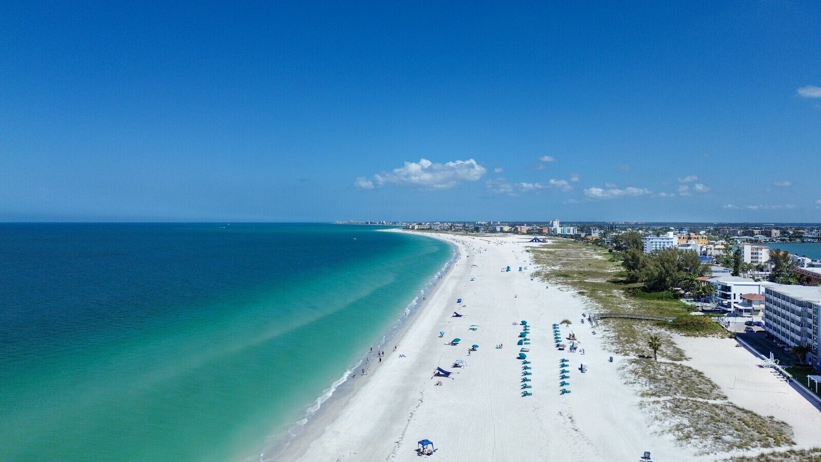 Une plage avec un ciel dégagé, un rivage sablonneux et des bâtiments en arrière-plan.