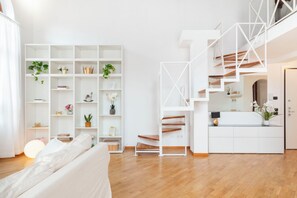 A modern interior with a white staircase, a white sofa, and a white shelving unit with plants.