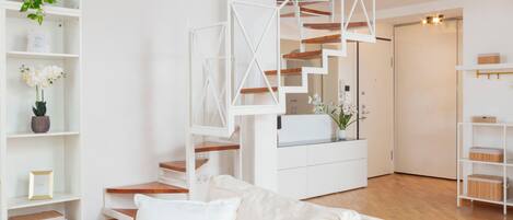 Un interior moderno con una escalera blanca, estanterías blancas y un sofá blanco.