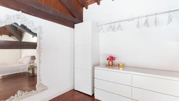 Una stanza con un letto bianco, un grande specchio decorativo, un armadio bianco e un tavolino con un vaso di fiori.