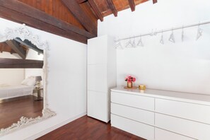 A room with a white bed, a large ornate mirror, a white wardrobe, and a small table with a vase of flowers.
