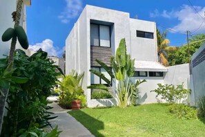 A modern building with a flat roof, large windows, and a well-maintained garden with various plants. - Downtown Cancún Studio · WiFi & Smart TV (Cancún)