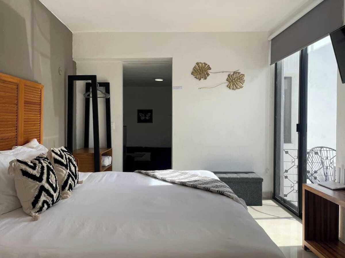 A modern hotel room with a large bed, a balcony with a view, and a sliding door leading to a hallway.