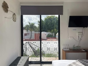 Ein Schlafzimmer mit einem Bett, einem an der Wand montierten Fernseher, einem Schreibtisch mit Stuhl und einem Balkon mit Ausblick.