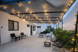 An outdoor seating area with chairs and tables, string lights overhead, and a view of a building in the background. - Downtown Cancún Studio · WiFi & Smart TV (Cancún)