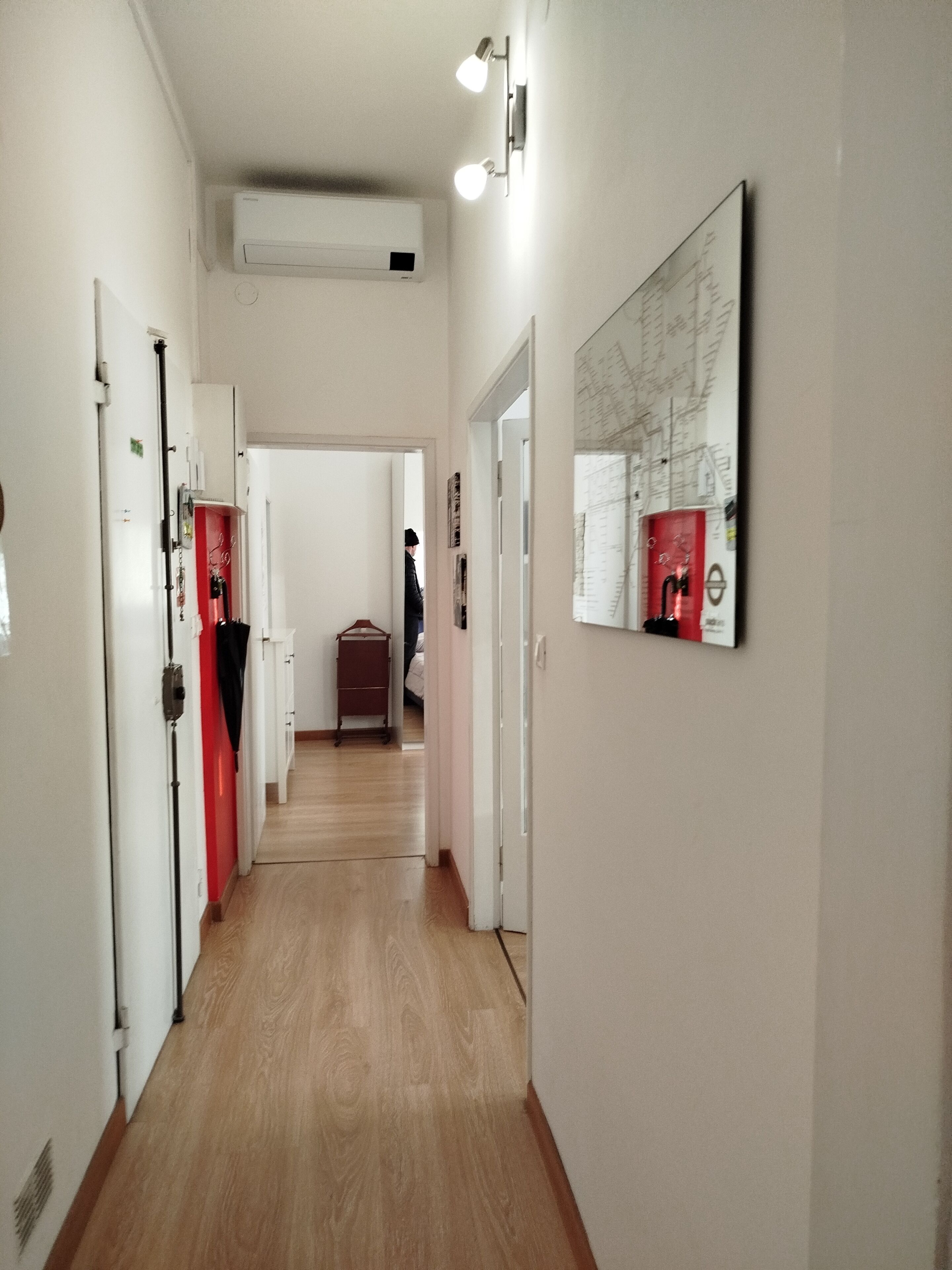 A hallway with wooden flooring, white walls, and a mounted air conditioner.