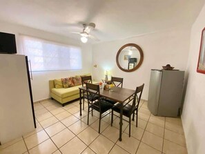 A dining area with a table and chairs, a sofa, a ceiling fan, a refrigerator, and a window with blinds. - Central 1BR Apt + Rooftop, Downtown Cancun (Cancún)