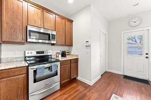 Una cocina con armarios de madera, electrodomésticos de acero inoxidable y una puerta blanca con un reloj.