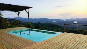 Una terraza de madera con una piscina rectangular y vistas a un paisaje montañoso.