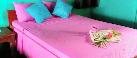 A bed with pink bedding and blue pillows, a wooden nightstand, and a small shelf with folded clothes.