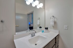Une salle de bain avec un lavabo blanc, un miroir avec éclairage intégré et deux serviettes suspendues à des porte-serviettes.