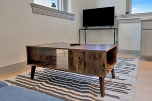 Un salon moderne avec une table basse en bois, un téléviseur à écran plat posé sur un meuble et un tapis à motifs.