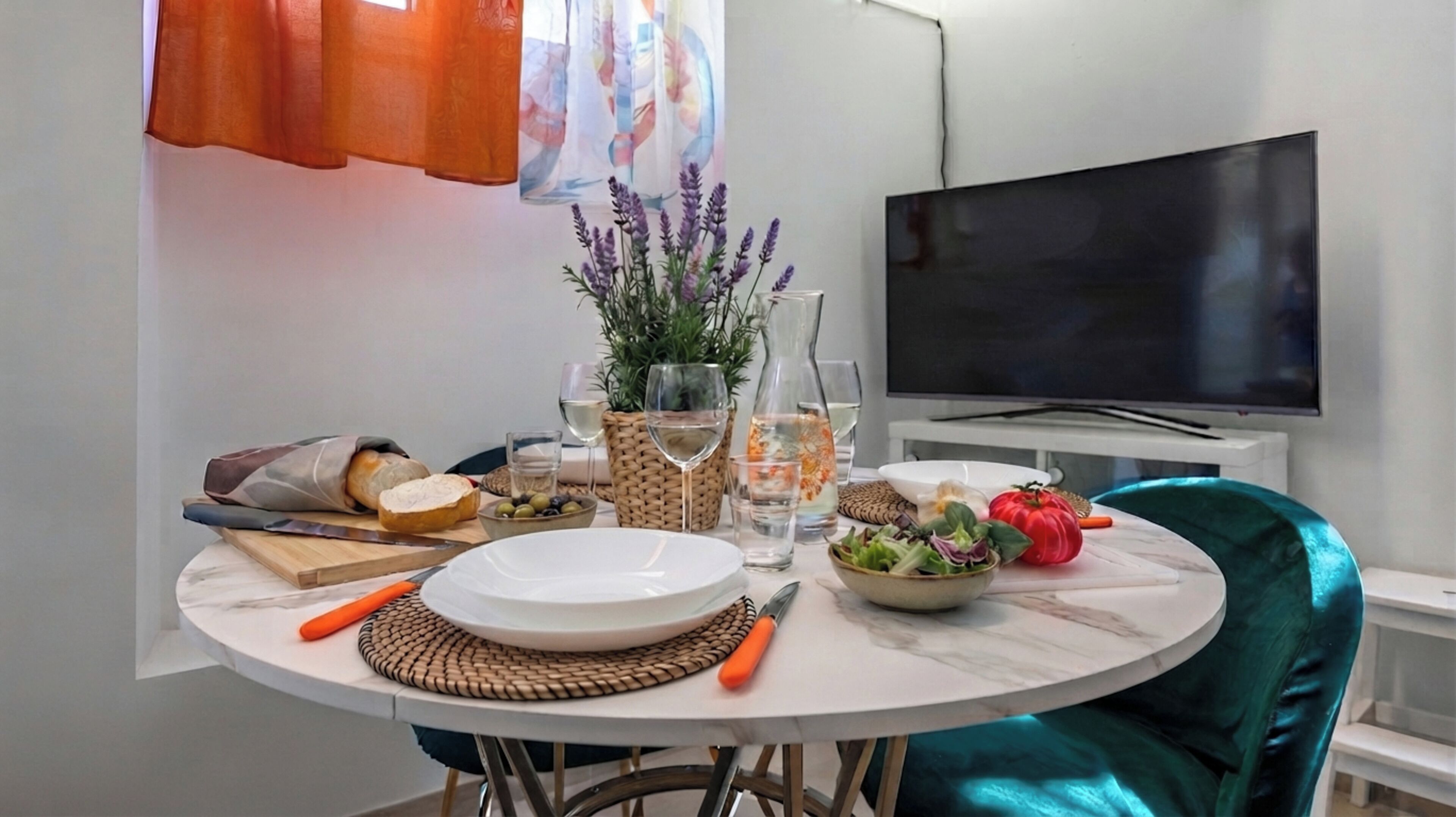 A dining area with a round table, a television, and various food items.