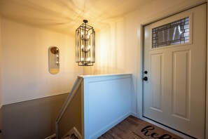 A hallway with a white door, a glass door with a grid pattern, a light fixture with multiple bulbs, and a mirror on the wall. - Luxury Apartment C on TU Campus and 2 miles to downtown (Tulsa)