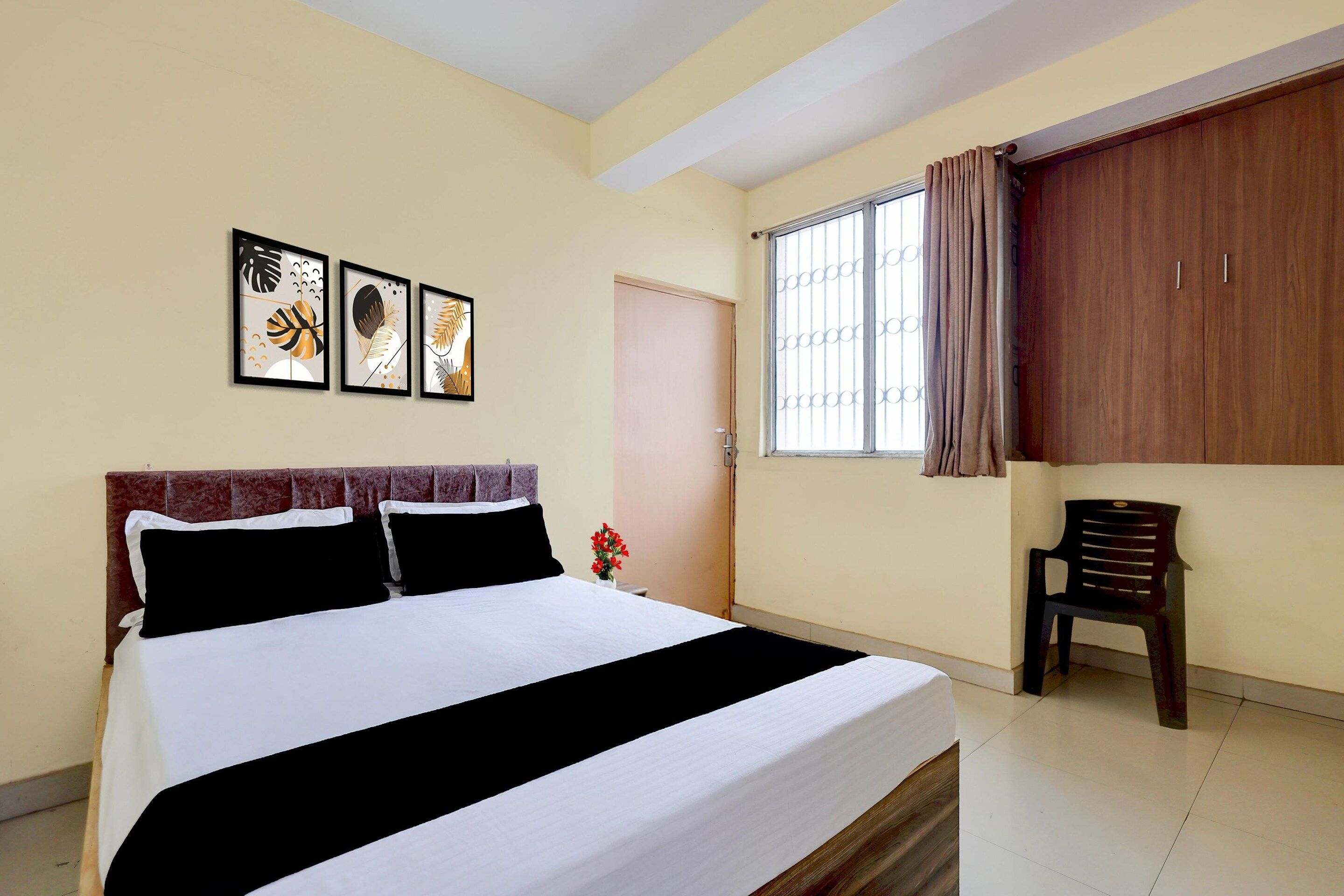 Habitación de hotel con cama, ventana con cortinas, una puerta y tres cuadros en la pared.