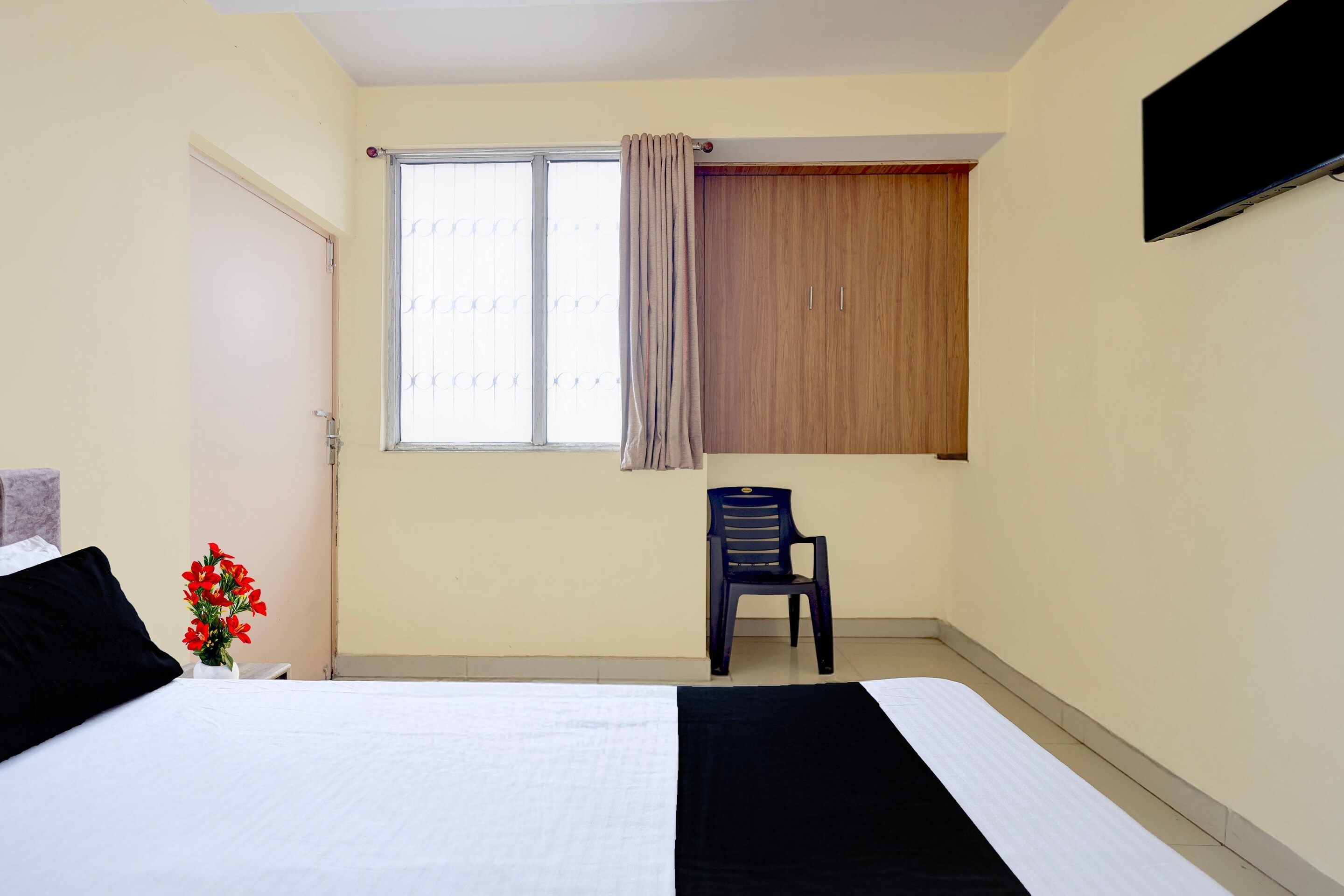A bedroom with a bed, a window with curtains, a chair, and a TV mounted on the wall.
