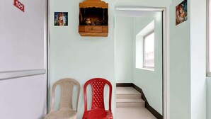 Un pasillo con dos sillas de plástico, un armario de madera con un objeto de latón y una escalera que lleva a otra habitación.