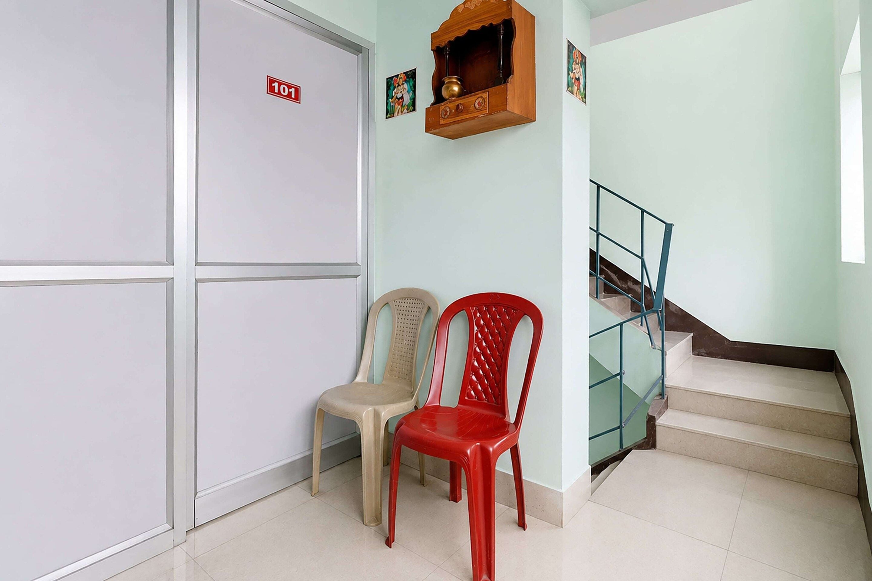 A hallway with a staircase, a door marked with the number 101, and two plastic chairs.