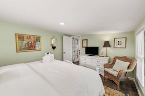 Un dormitorio con cama, cómoda, televisor, silla y puerta que da a otra habitación.