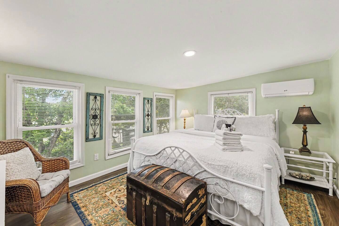 A bedroom with a bed, bedside tables, a lamp, a chair, a bench, and a window with blinds.