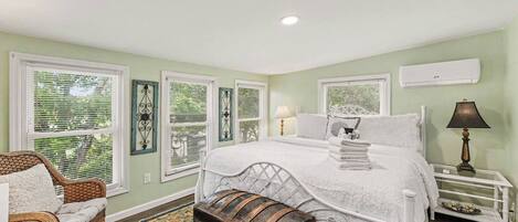 A bedroom with a bed, bedside tables, a lamp, a chair, a bench, and a window with blinds.