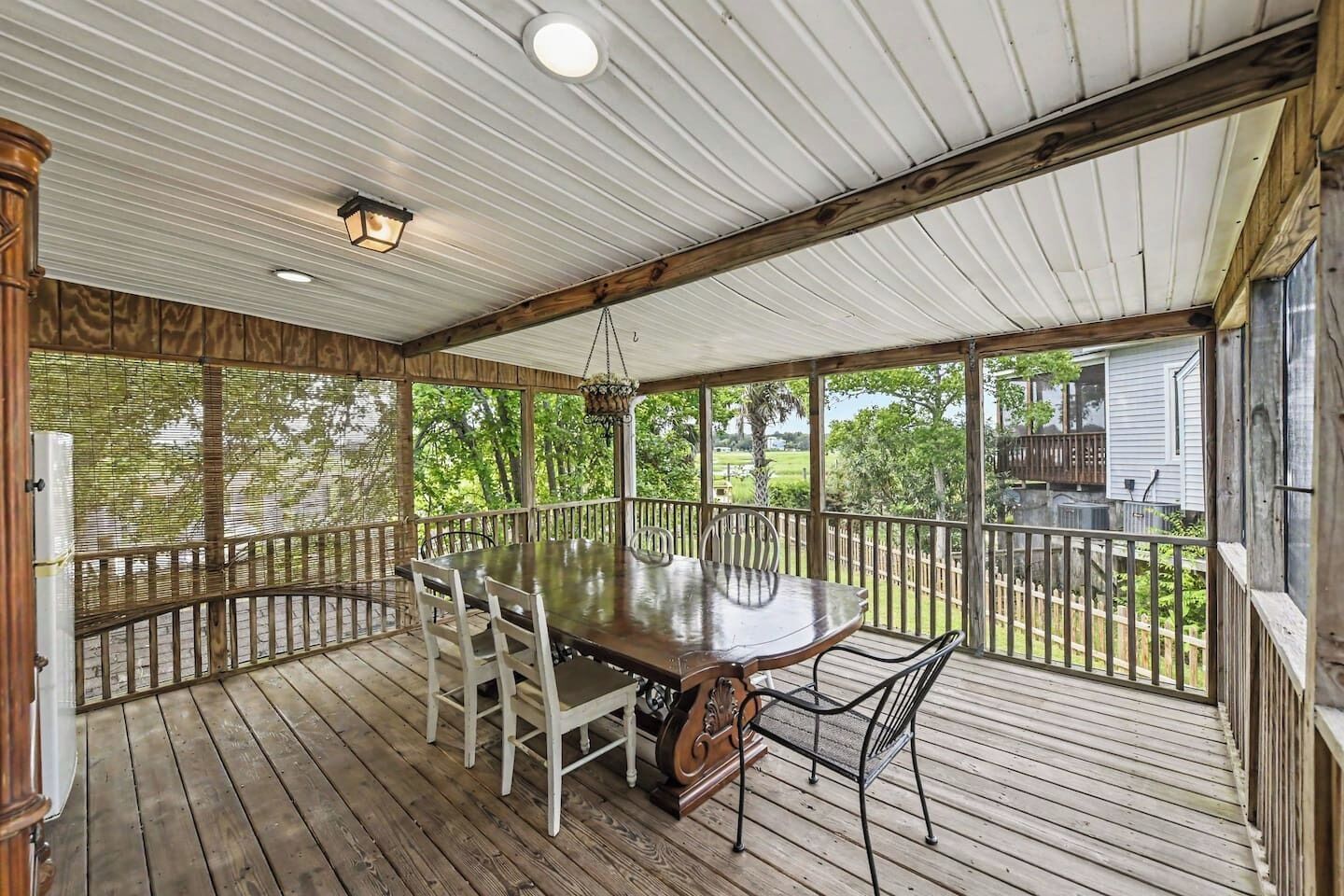 A covered outdoor deck with a wooden table and chairs, surrounded by a wooden railing.