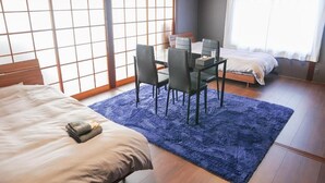 A room with a bed, a dining table with chairs, a small table with a chair, and a window with a view.