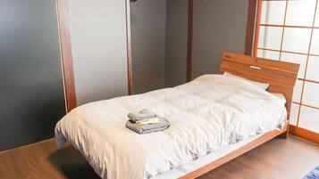 A single bed with a wooden headboard, a grey towel, and a white bedsheet in a room with wooden flooring and a sliding door closet.