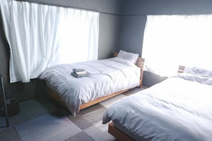 A hotel room with two beds, a window with curtains, and a small bedside table.