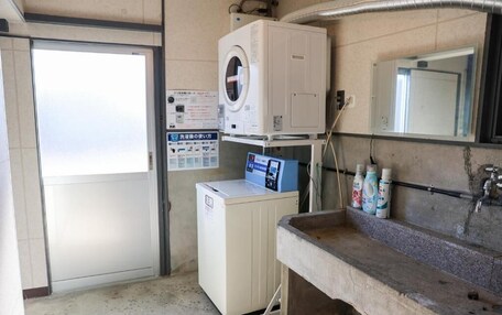 A laundry room with a washing machine, a dryer, a sink with bottles, and a mirror.