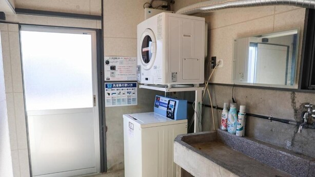 A laundry room with a washing machine, a dryer, a sink with bottles, and a mirror.