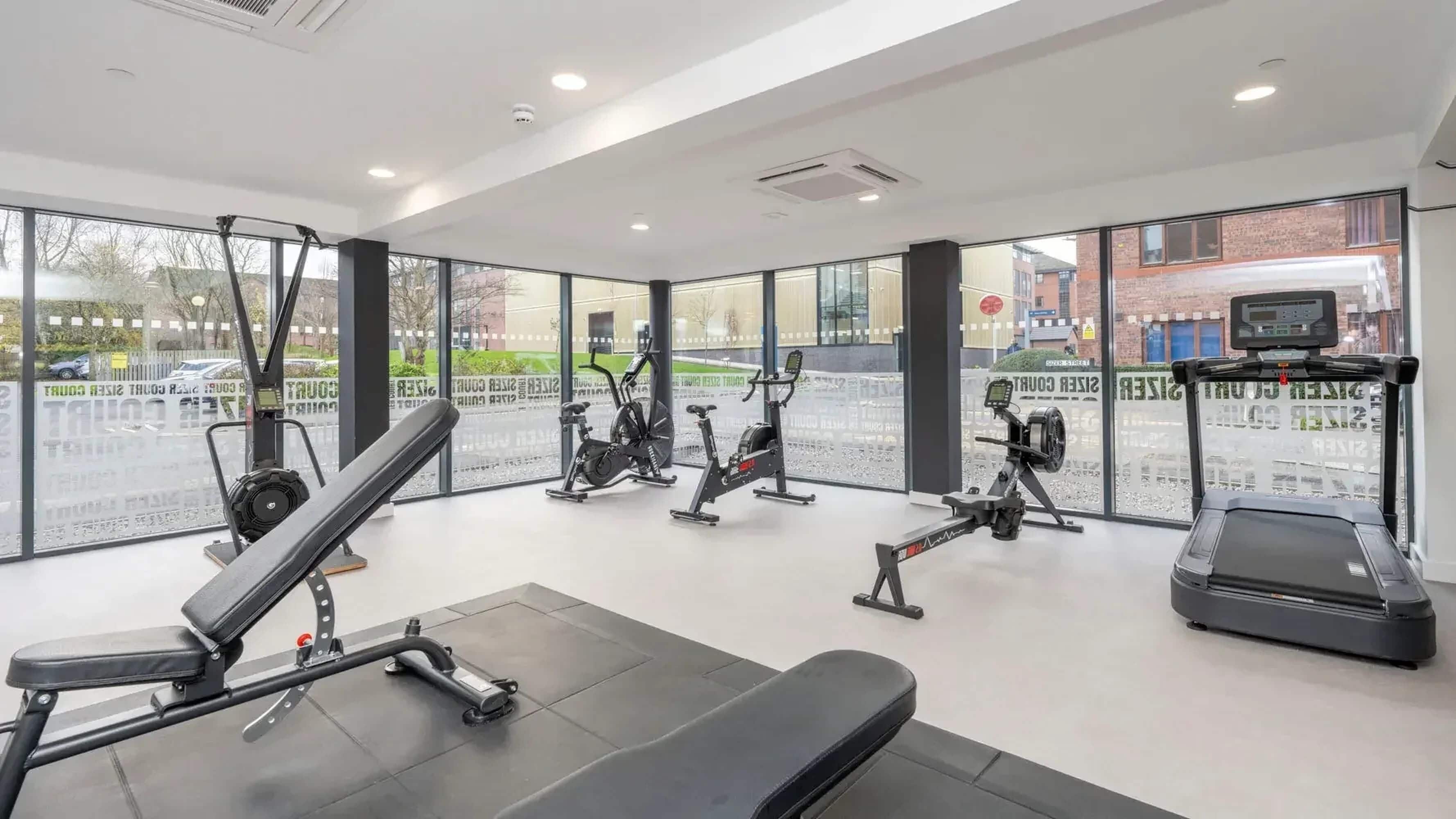 Ein Fitnessstudio mit unterschiedlichen Trainingsgeräten, großen Fenstern und Blick auf die Straße.