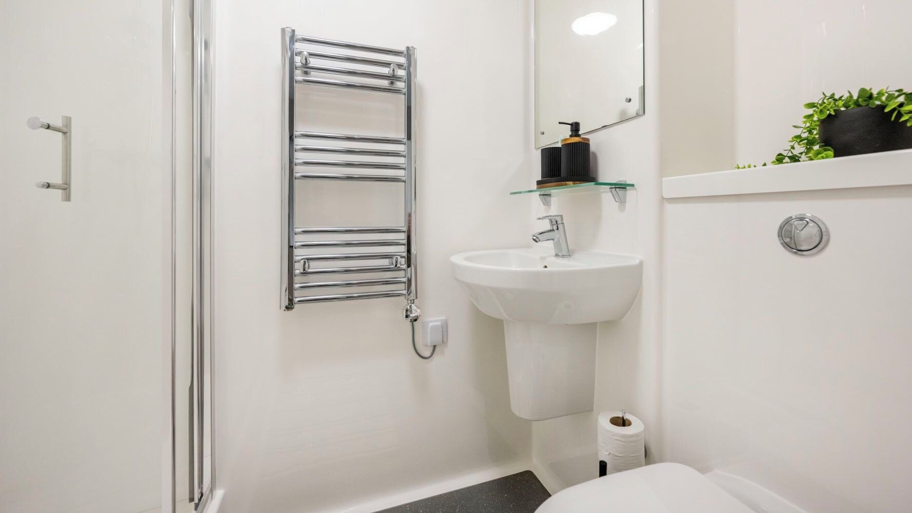 A bathroom with a chrome towel rack, a white sink, a mirror, and a toilet.