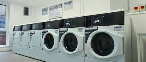 A laundry facility with multiple washing machines and dryers, control panels, and instructional posters on the wall.