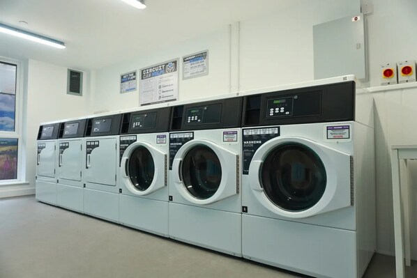A laundry facility with multiple washing machines and dryers, control panels, and instructional posters on the wall.