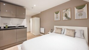 A bedroom with a large bed, a nightstand, and a wall-mounted lamp. - Student Only Sizer Court (Preston)