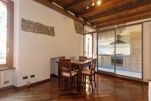 Ein Essbereich mit einem Holztisch und Stühlen, einer Steinwand und Blick auf eine moderne Küche durch eine Glastür.