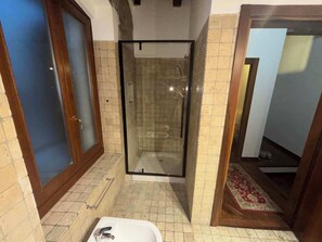 Ein Badezimmer mit einer Duschkabine, einem weißen Waschbecken und einem Fliesenboden.