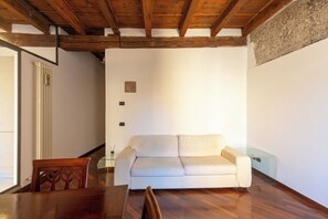 Quarto com teto de madeira, sofá branco, mesa de vidro e uma cadeira.