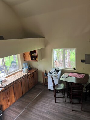 A kitchen with a stove, a table with chairs, wooden cabinets, and a window with a view of trees.