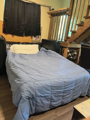 A bed with a blue quilt, a wooden chair, a wooden table, and a staircase. - Retreat to this quiet 1 bedroom cabin in the woods near a lake. (Wasilla)