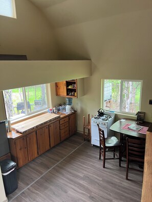 A kitchen with wooden cabinets, a stove, and a dining area with chairs. - Retreat to this quiet 1 bedroom cabin in the woods near a lake. (Wasilla)