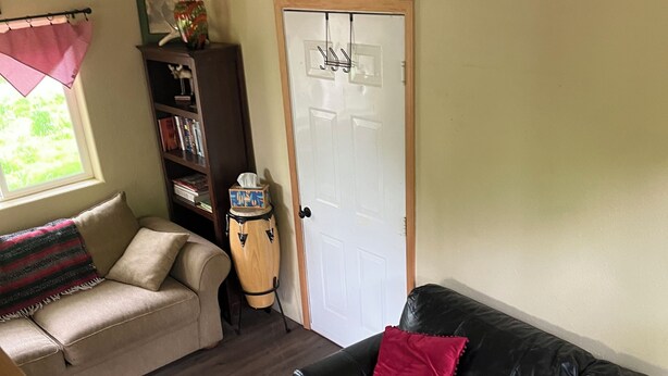 A living room with a black leather sofa, a beige sofa, a wooden coffee table with a chessboard, a bookshelf, and a door with a white frame. - Retreat to this quiet 1 bedroom cabin in the woods near a lake. (Wasilla)