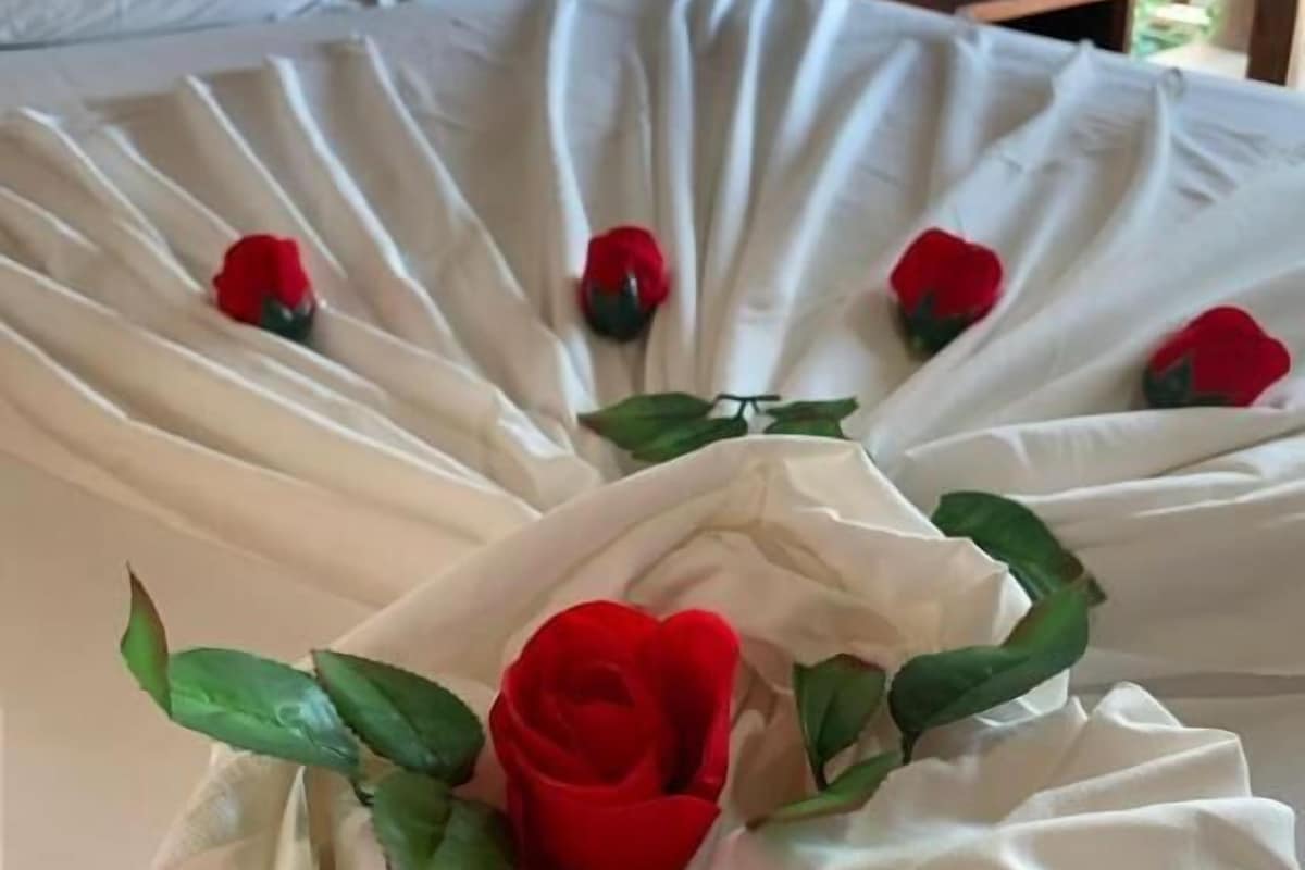 Un letto con lenzuola bianche e rose rosse disposte a ventaglio.