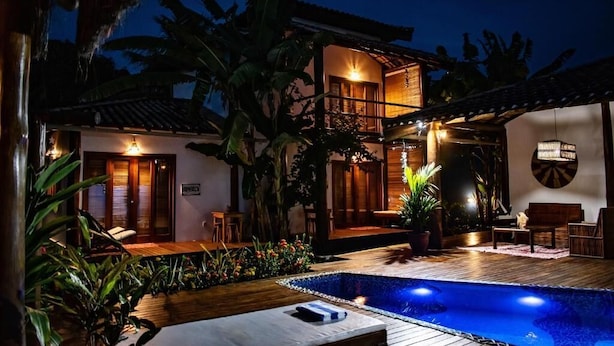 A two-story building with a swimming pool, outdoor seating, and tropical plants. - Pousada Barra Suítes (Maraú)