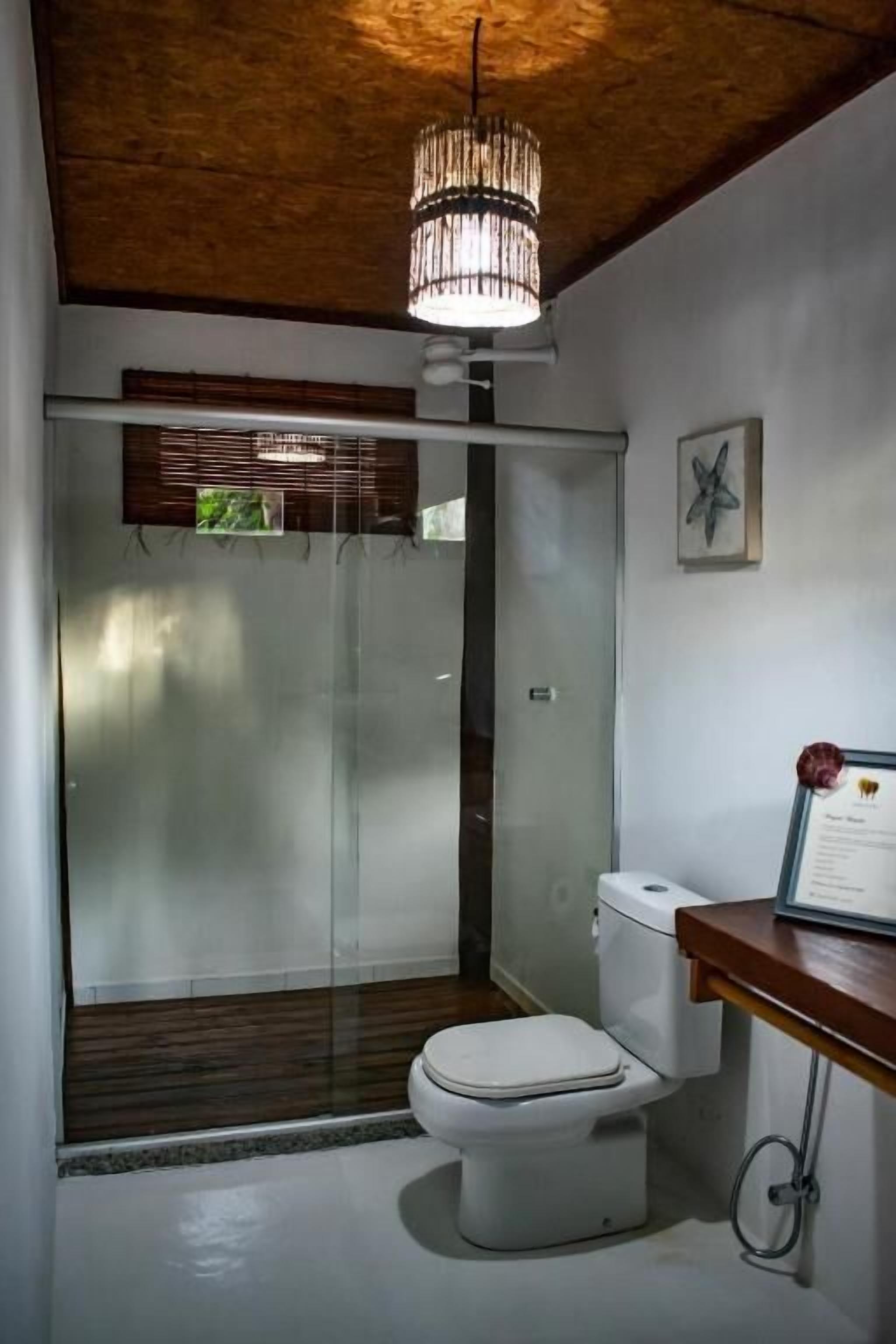 A bathroom with a toilet, a shower enclosure, a wooden ceiling, and a wall-mounted light fixture.