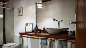 Un baño con inodoro blanco, tocador de madera con lavamanos, espejo y toallas colgadas en un perchero.